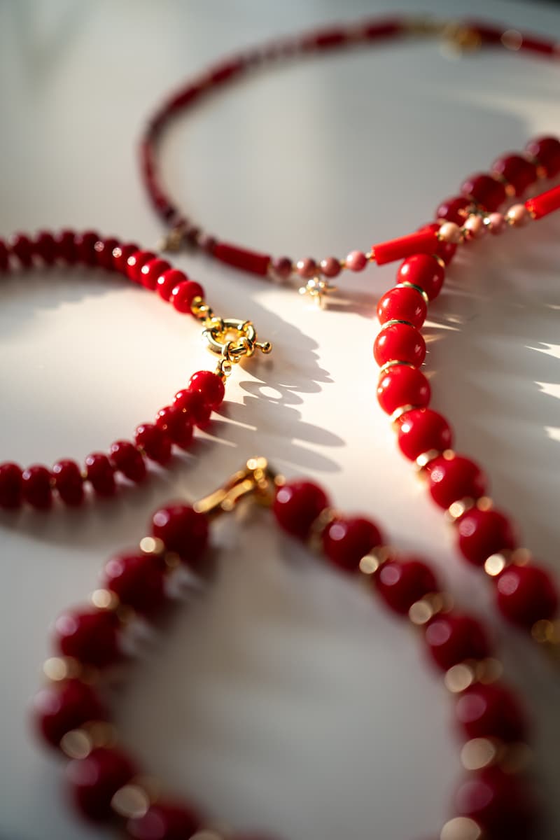 Red Coral beaded jewelry set, including multiple bracelets and a necklace with gold accents, displayed in soft, bright light to highlight the texture and vibrant color.