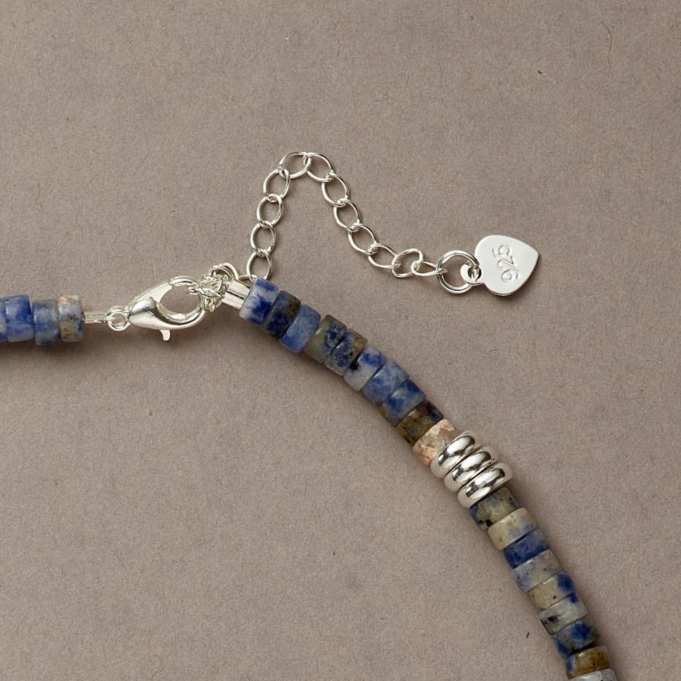 Zoomed-in view of Blue Mind necklace clasp with silver spacer and deep blue stone on warm beige surface.