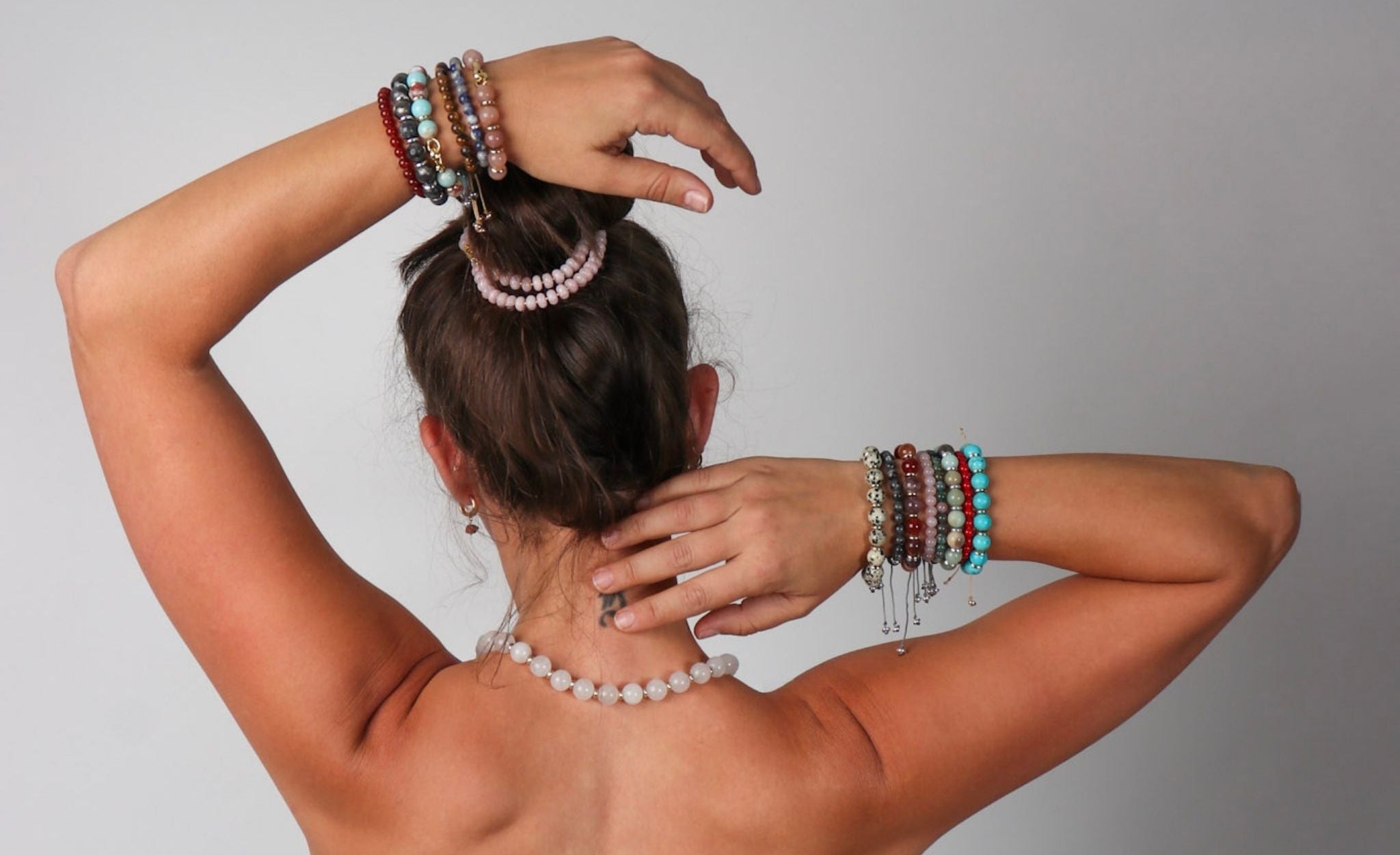 Person with multiple bracelets on arms and a necklace, against a plain background