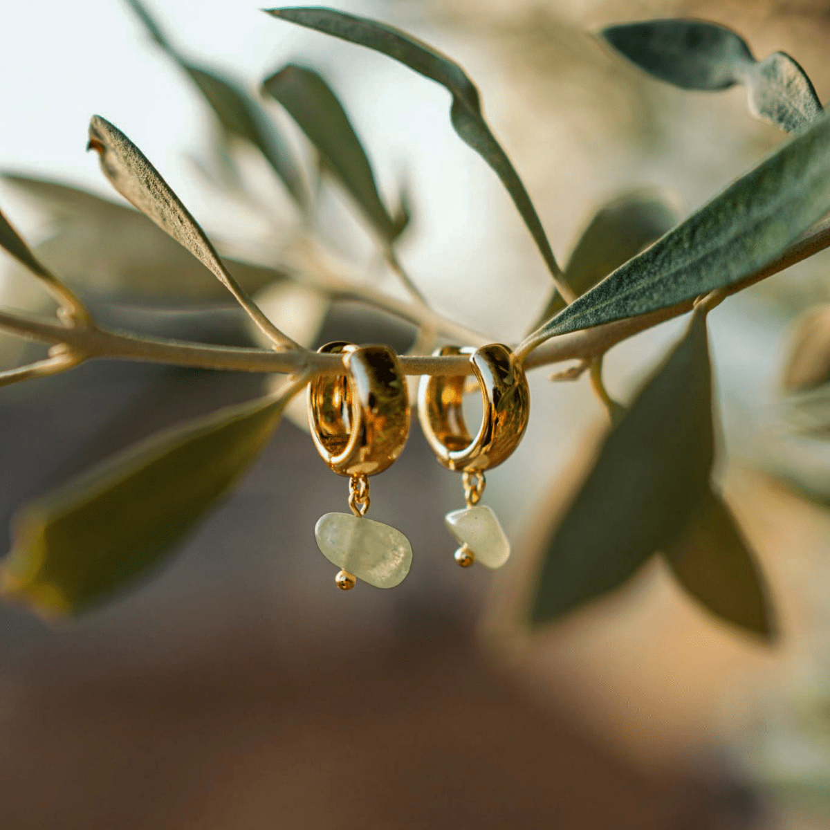 Gold hoop earrings with green beads on an olive branch