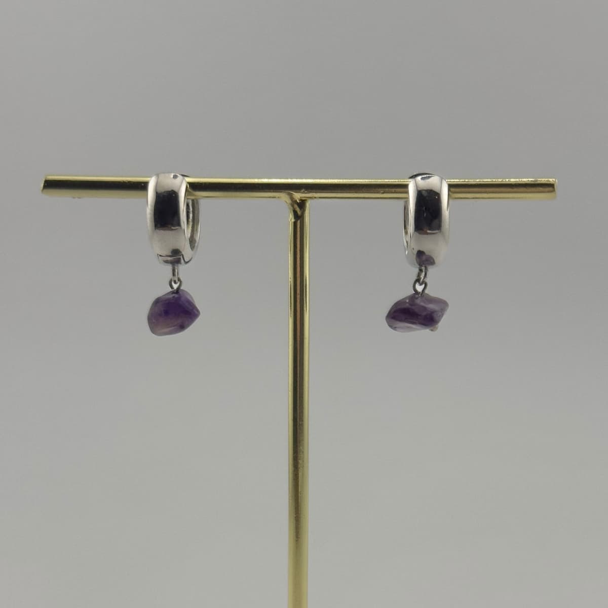 Pair of silver earrings with purple gemstones on a gold stand against a gray background