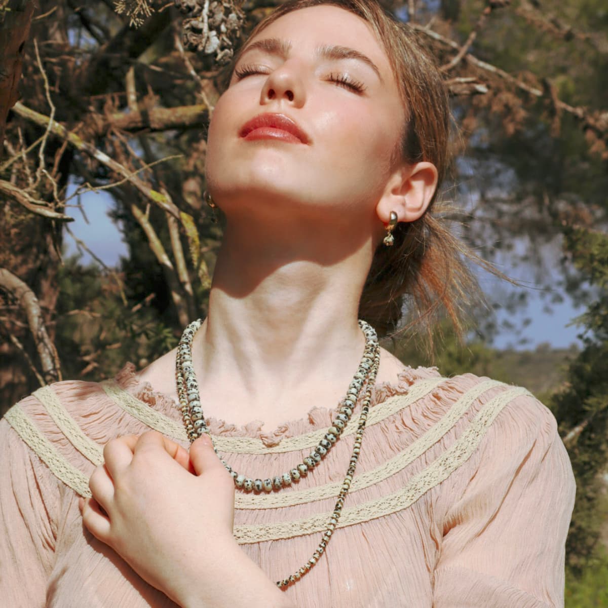 Woman wearing a necklace outdoors with trees in the background