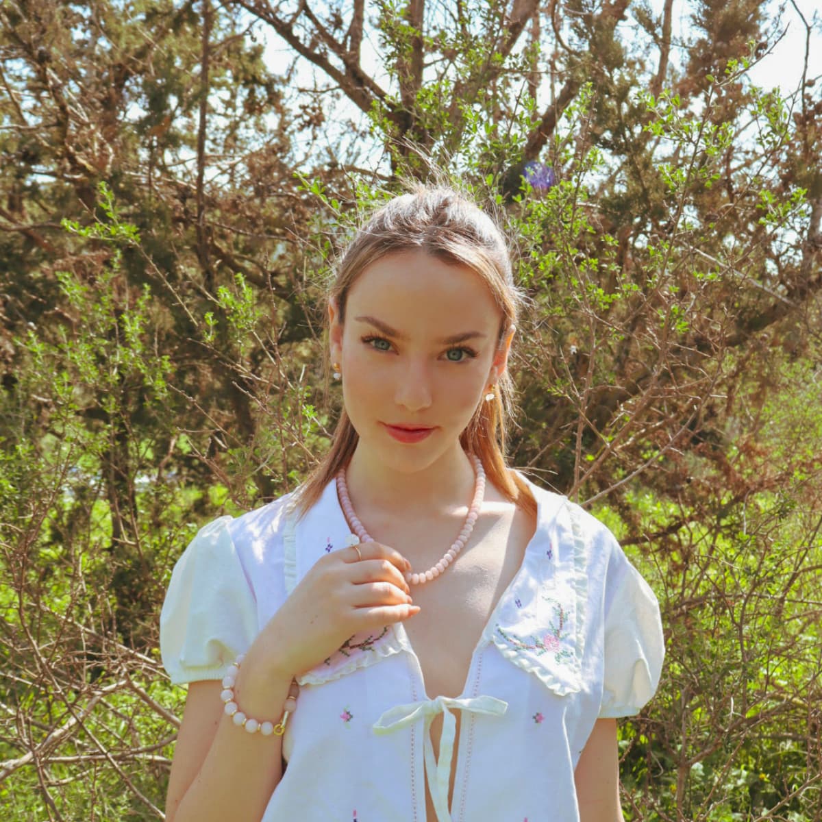 Woman in a white dress with a pink necklace standing in a forest