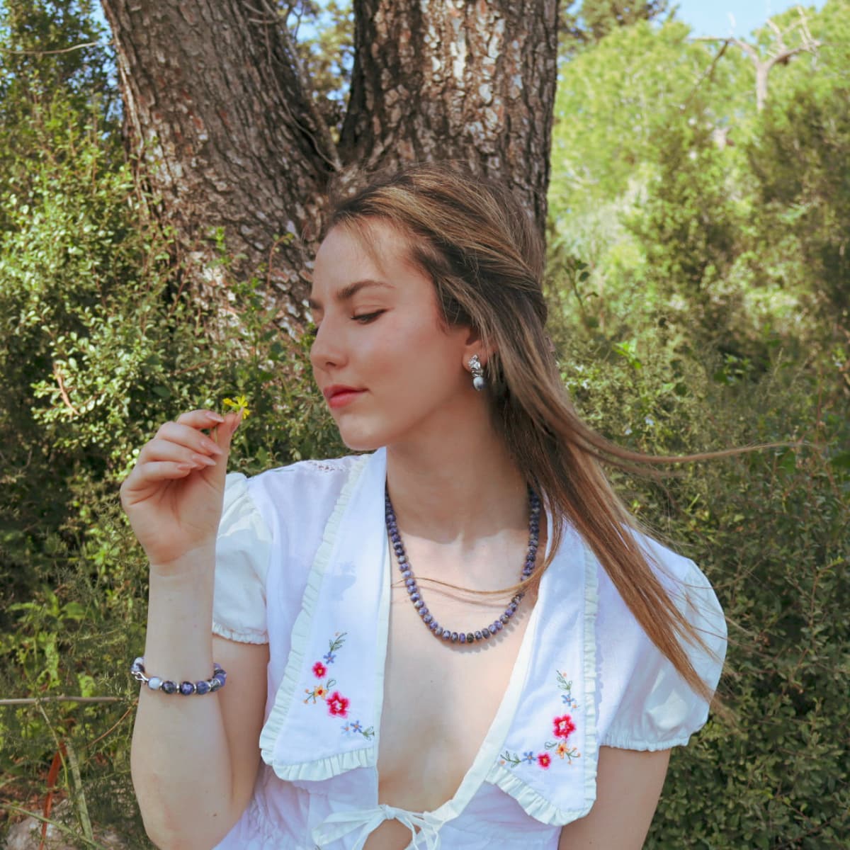 Woman in a white embroidered dress standing outdoors with trees in the background