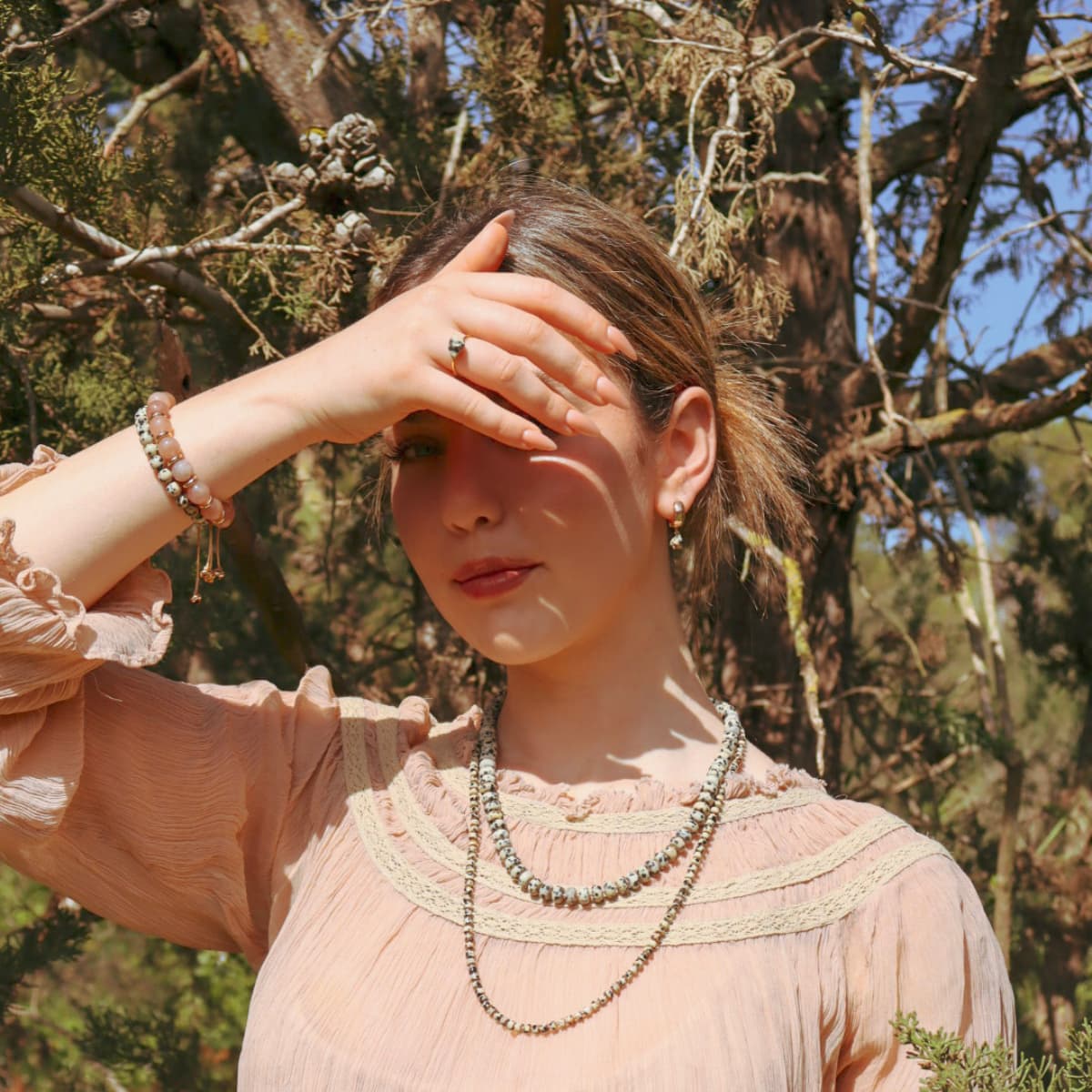 Woman in a pink blouse with a necklace standing in a forest