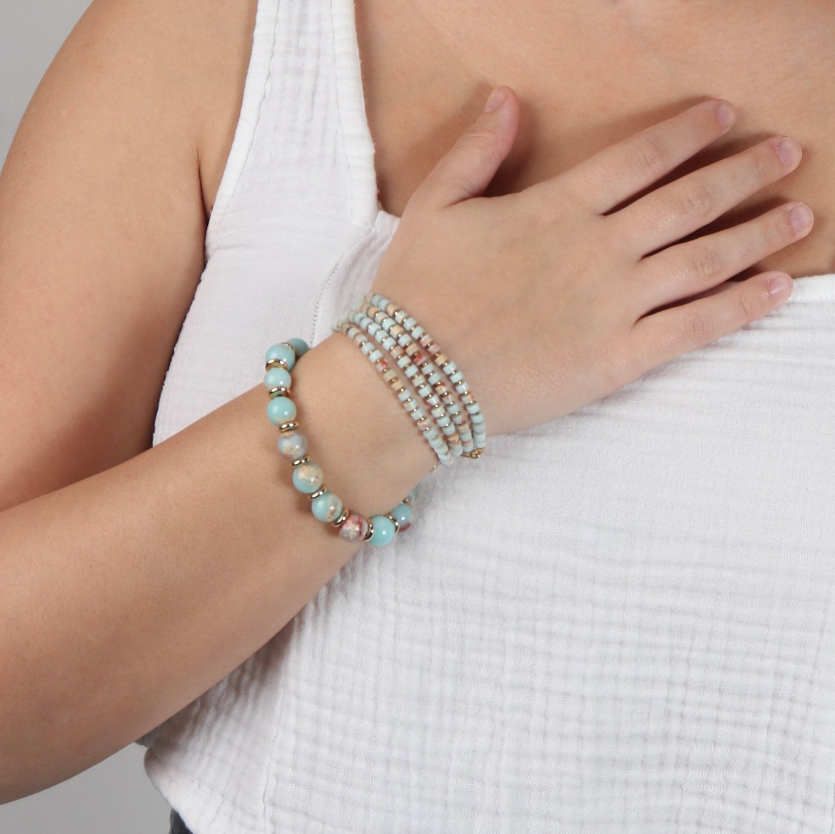 Person wearing multiple bracelets on a plain background