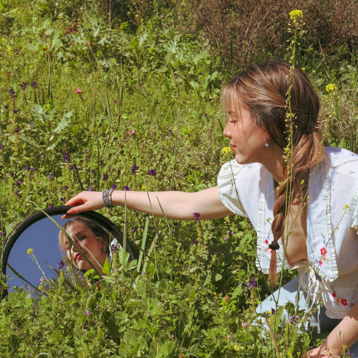 Woman holding a mirror reflecting a child amidst greenery