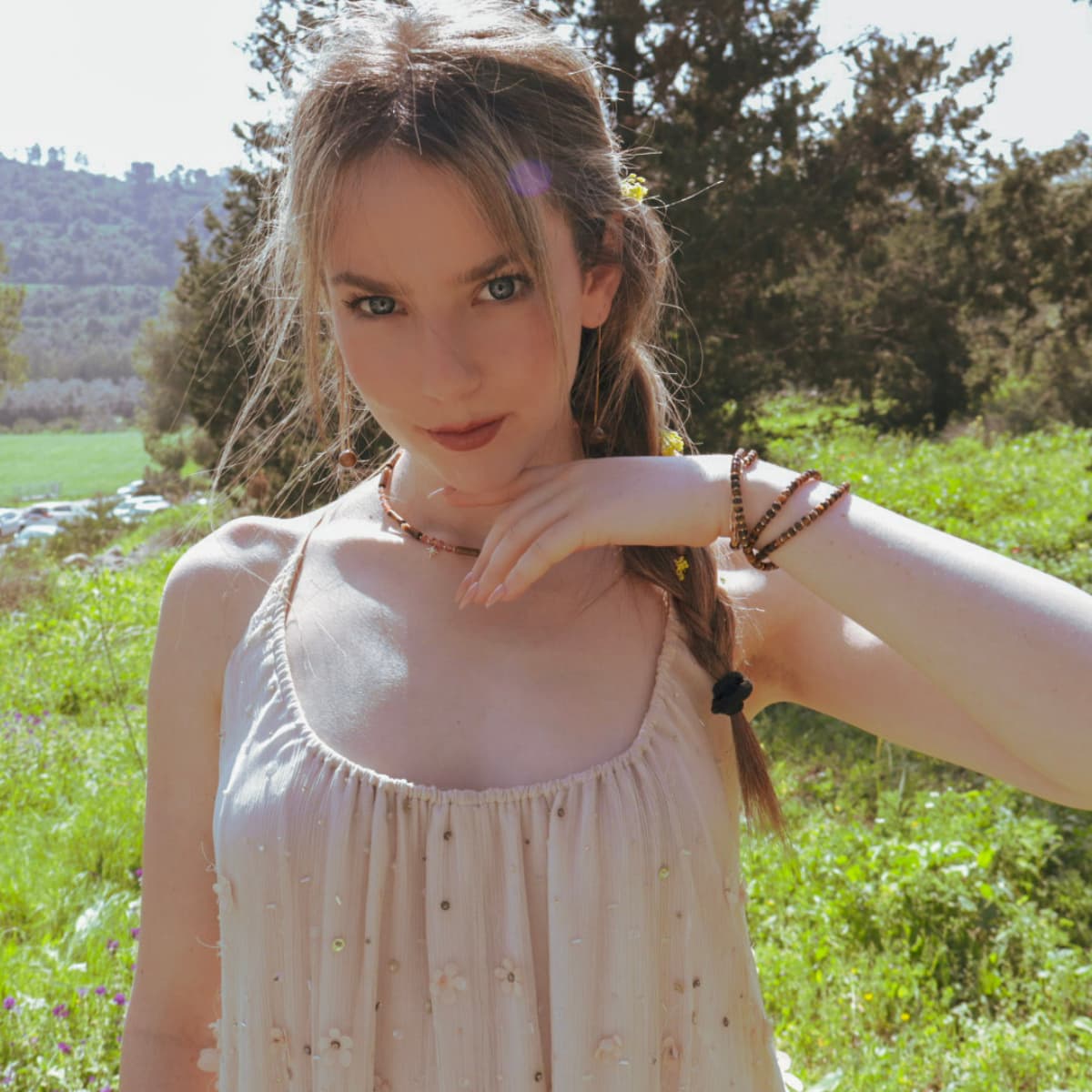Woman in a light dress standing in a grassy field with trees in the background