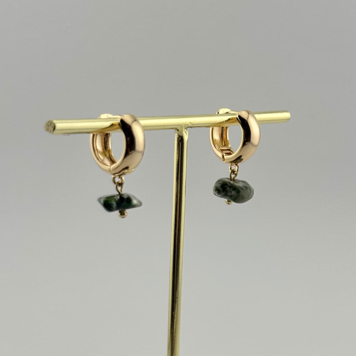 Gold earrings with green stones on a gray background
