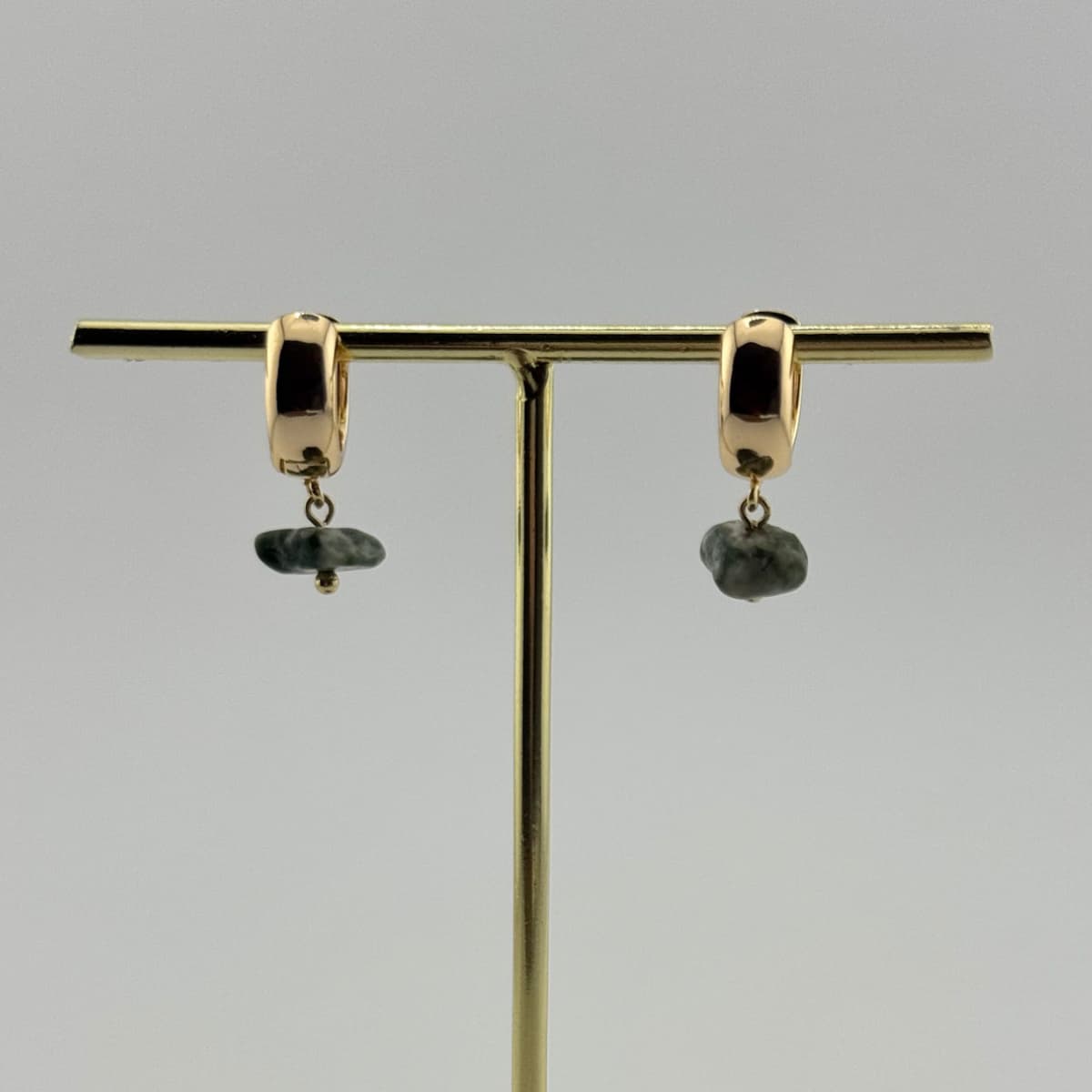 Gold hoop earrings with green stones on a gold stand against a gray background