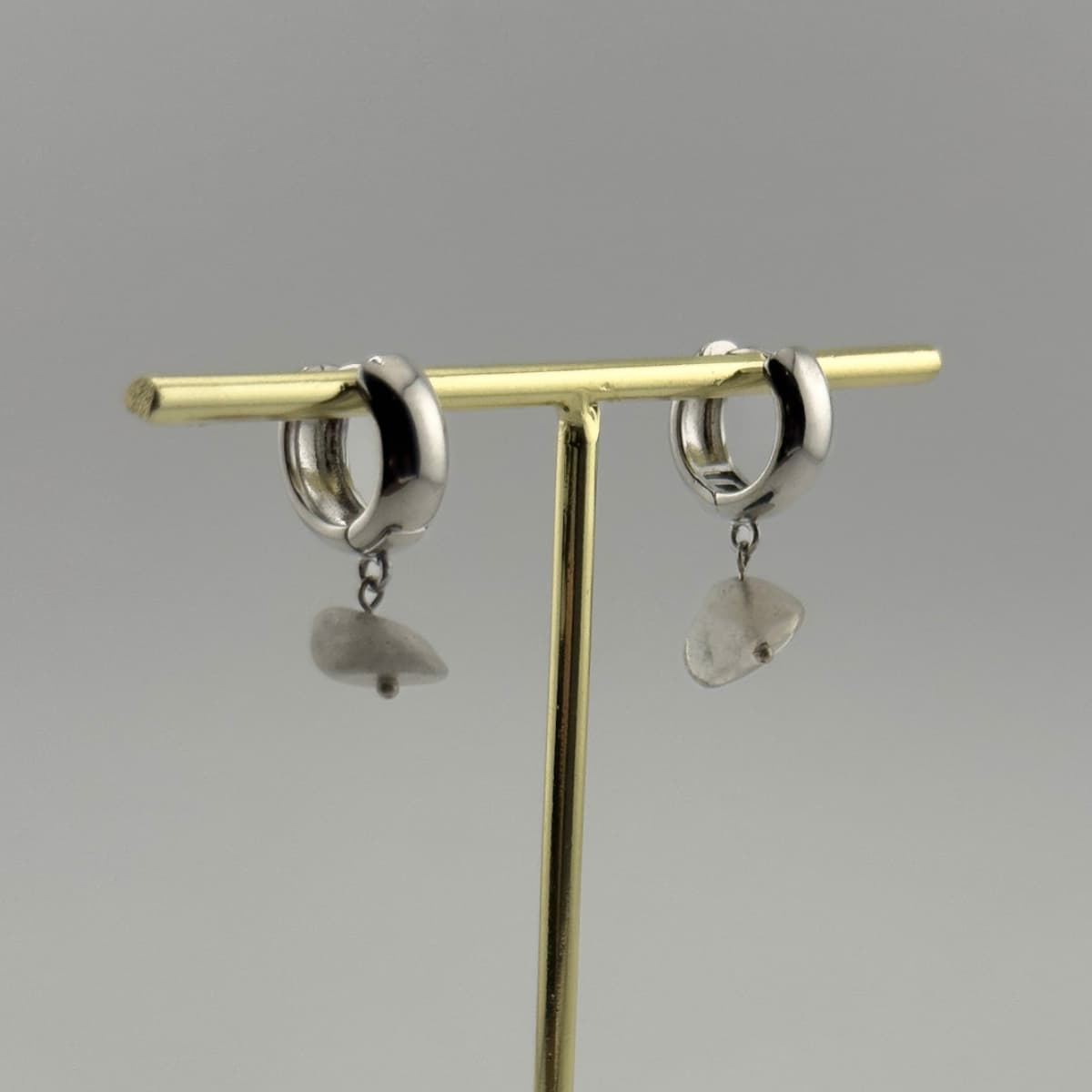Pair of silver hoop earrings with heart-shaped charms on a gold T-shaped stand against a gray background.