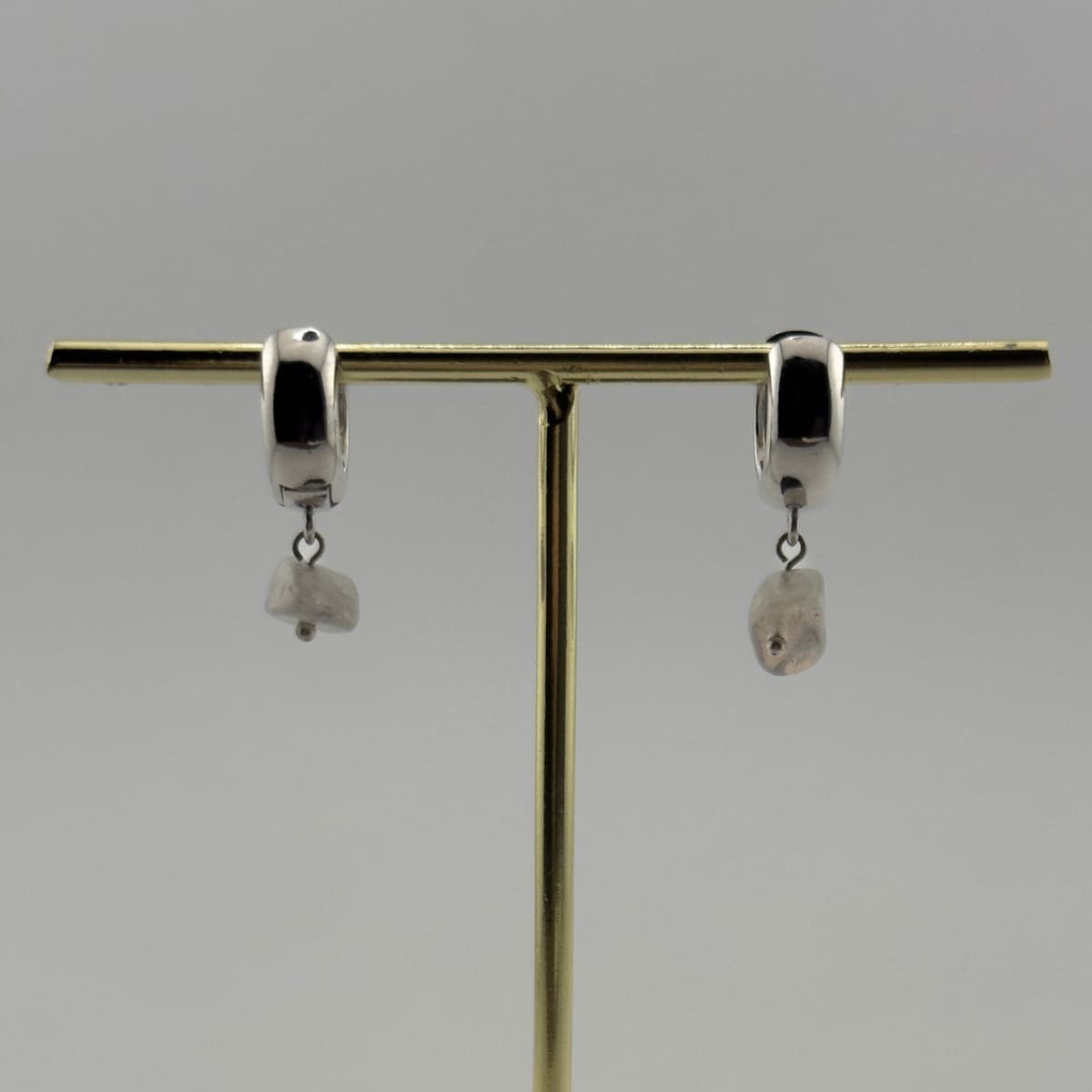 Pair of silver hoop earrings with dangling stones on a gold stand against a gray background
