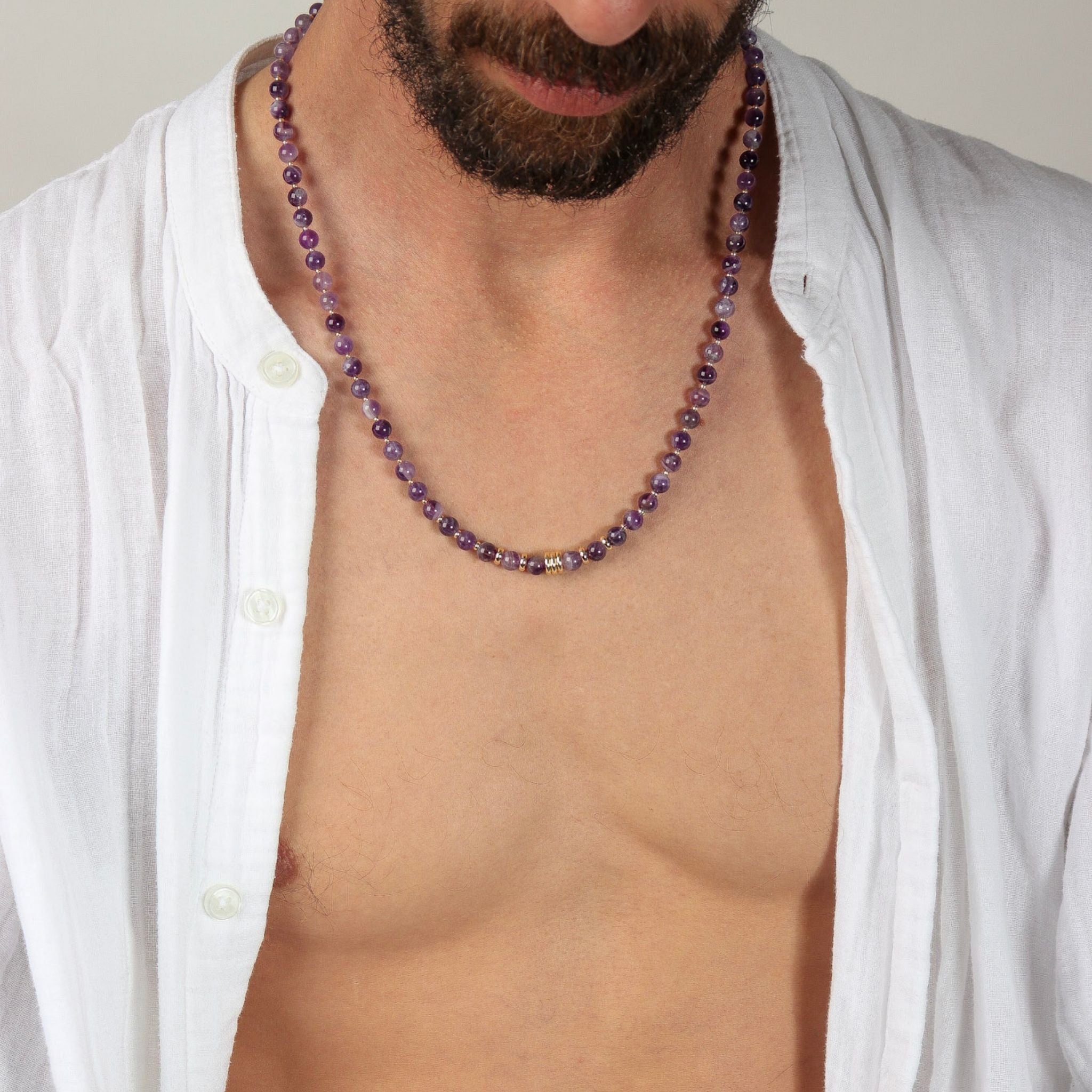 Man wearing a purple beaded necklace with a white shirt open