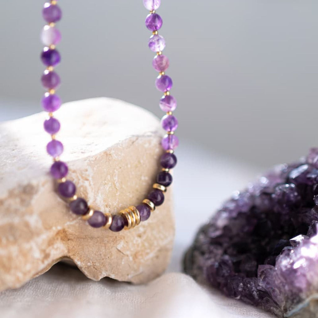 Purple beaded necklace on a rock with a purple crystal formation