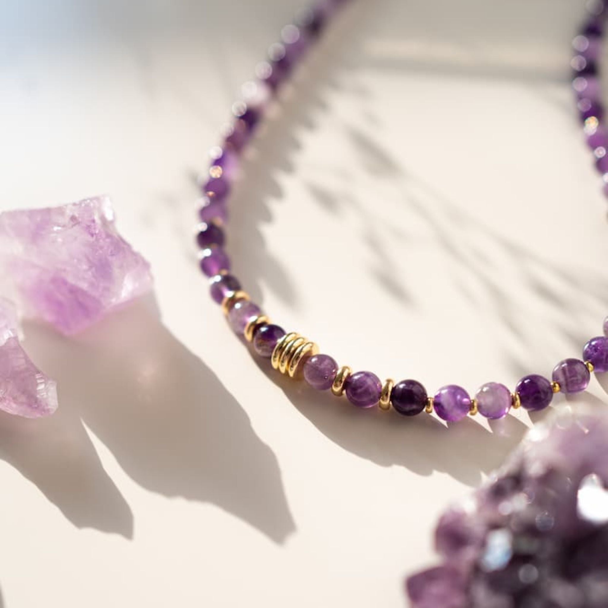 Purple beaded bracelet with gold accents on a white surface with purple crystals.