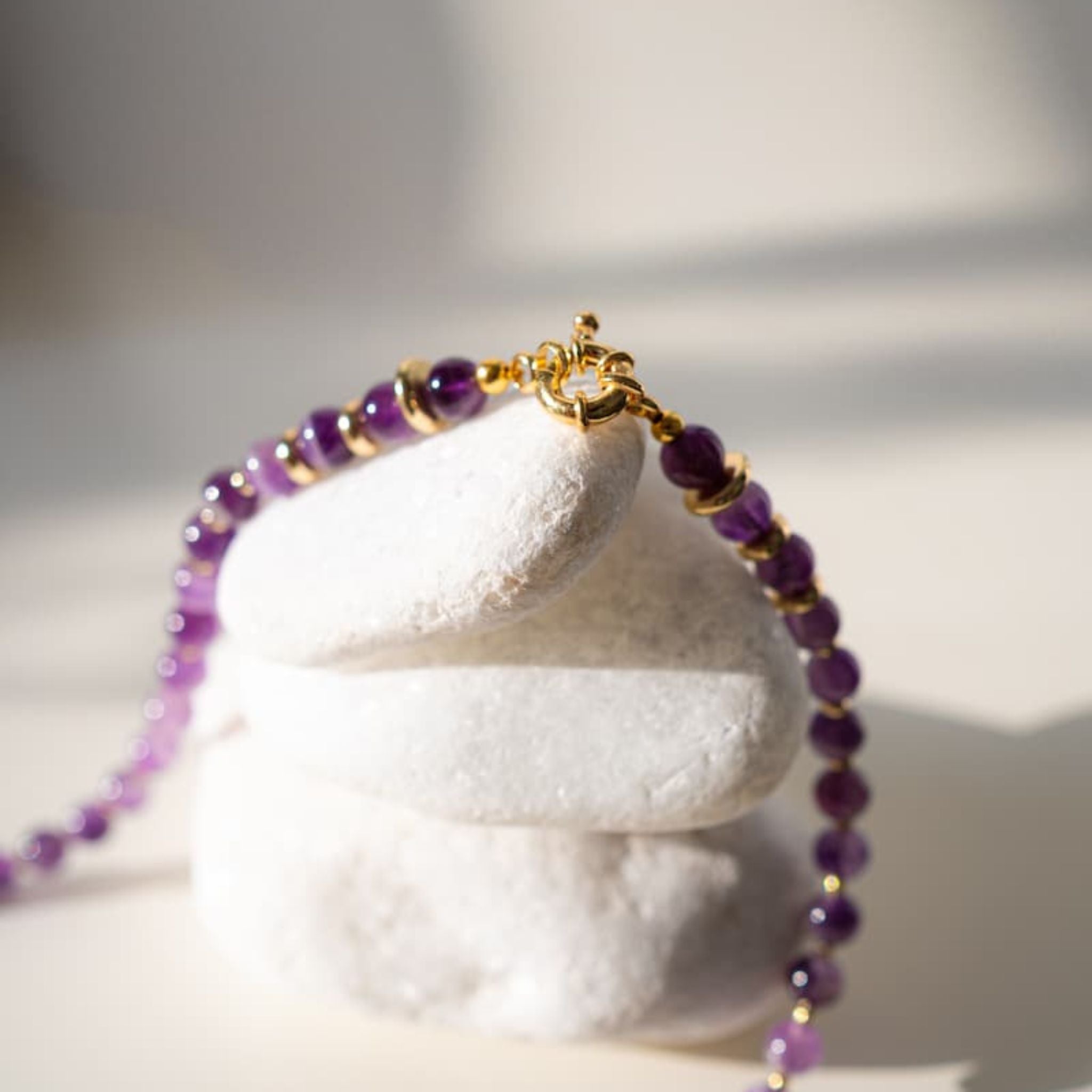 Purple beaded bracelet with gold accents on a white stone stand