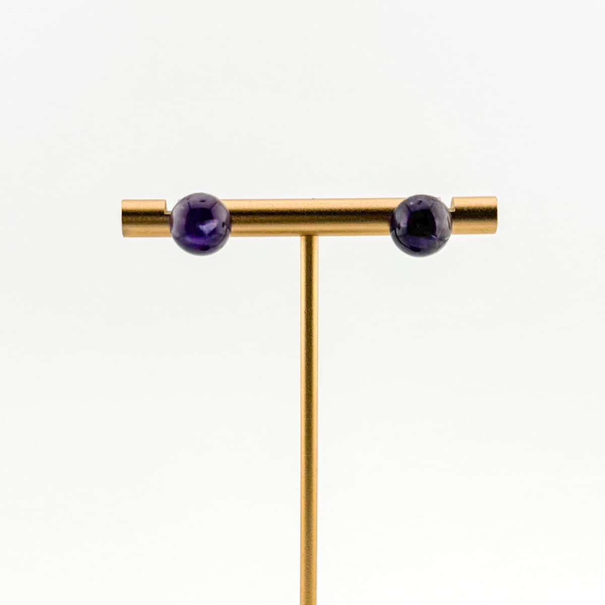 Gold T-bar earring with purple gemstones on a white background