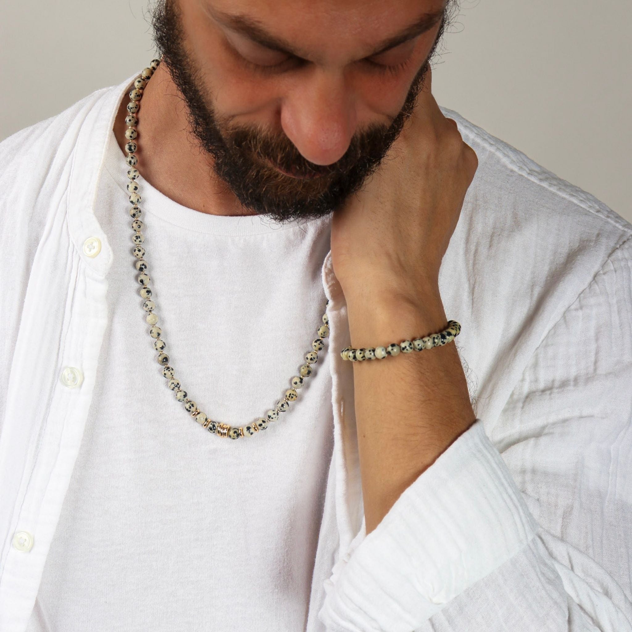 Man wearing a necklace and bracelet, looking down.