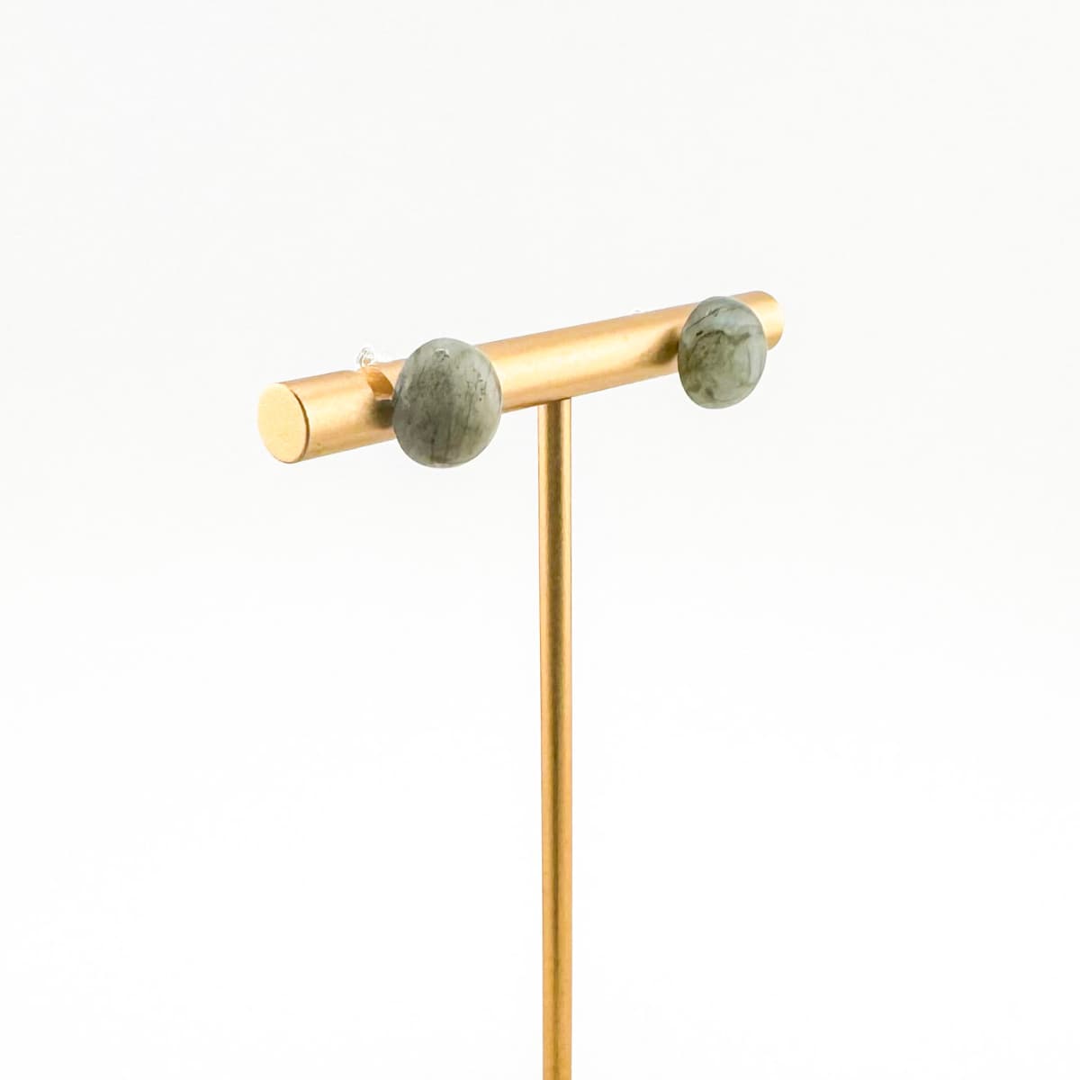 Gold earring stand with two green gemstones on a white background