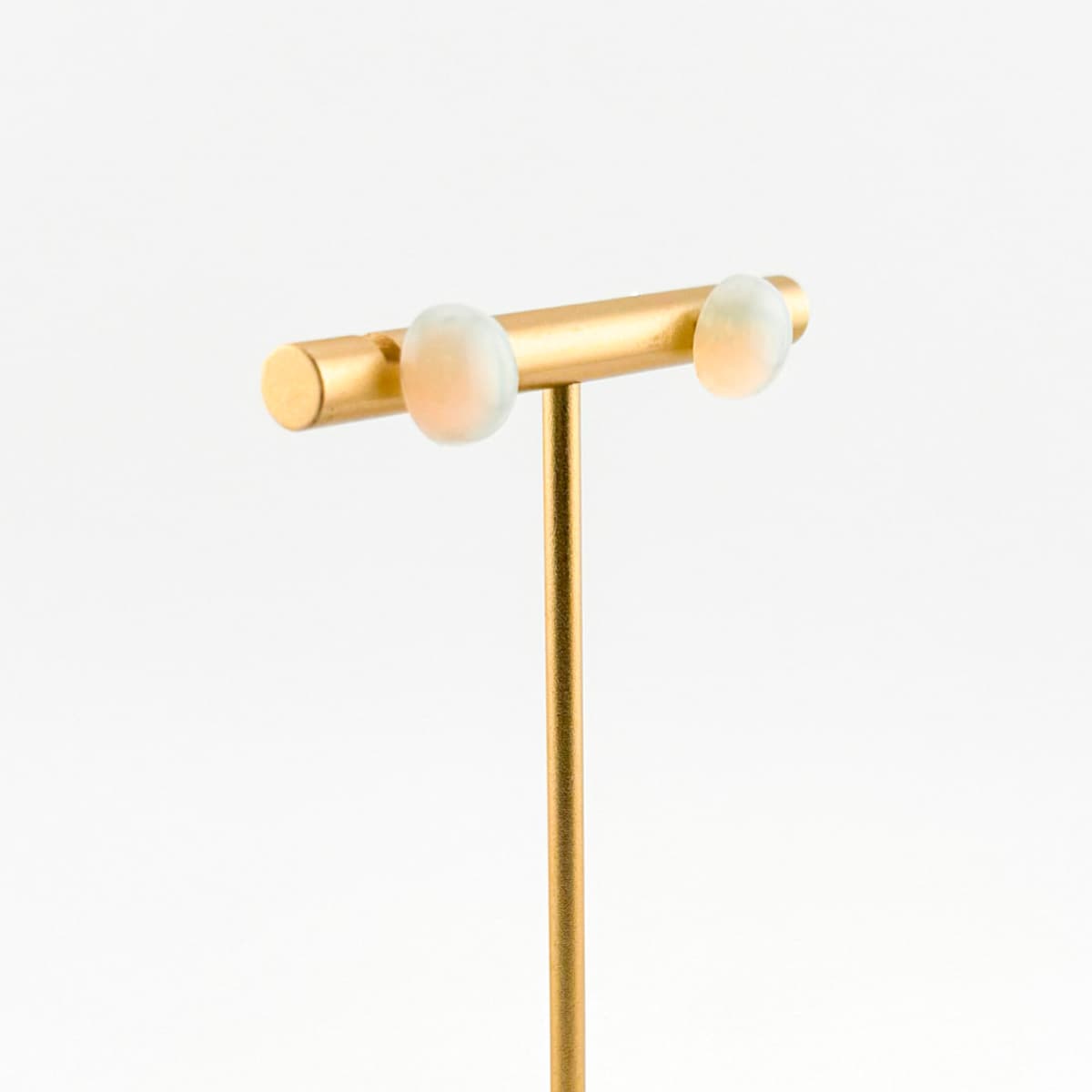 Gold earring with two white stones on a light gray background