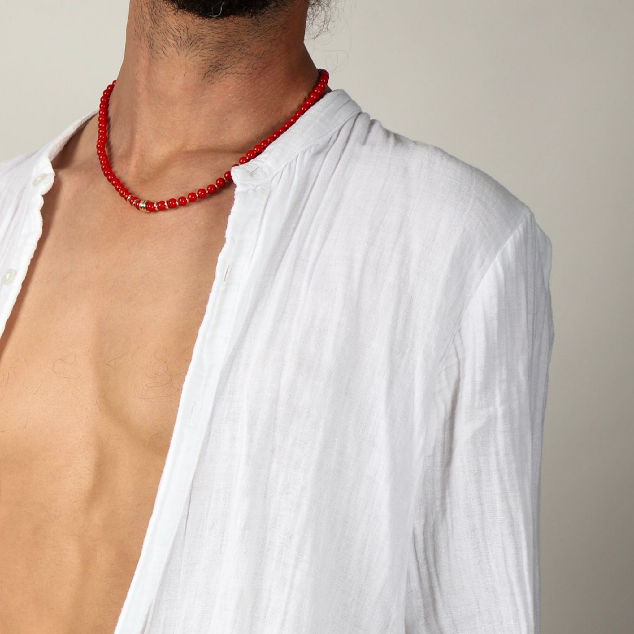 Person wearing a red beaded necklace and a white shirt against a neutral background