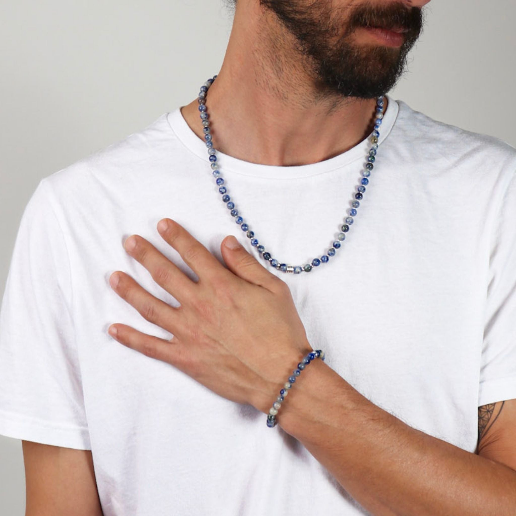 Man wearing a blue beaded necklace and bracelet on a plain background