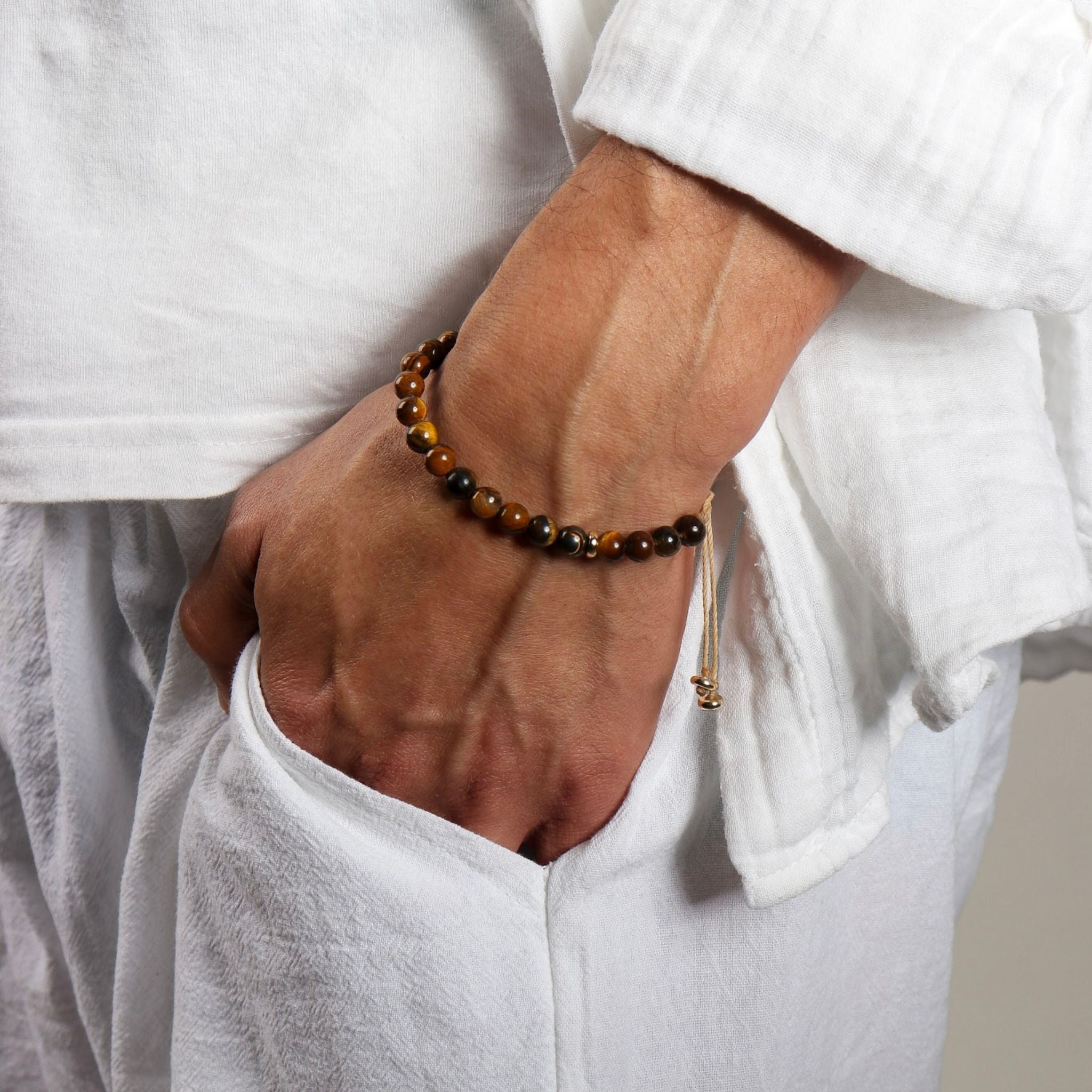 Person wearing a brown beaded bracelet on a plain background