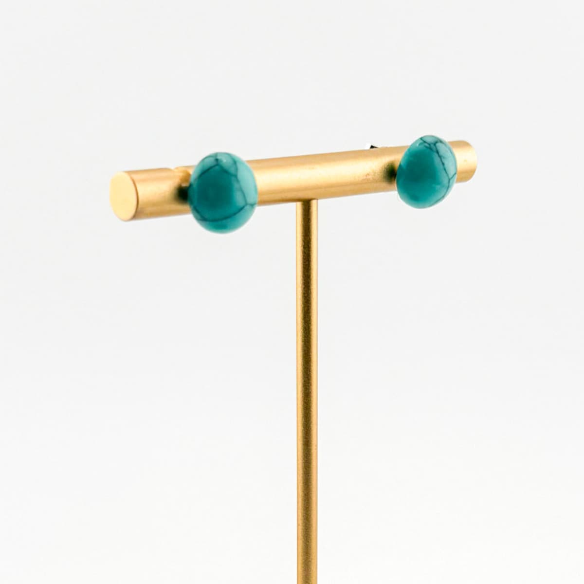 Gold earring with teal gemstones on a white background