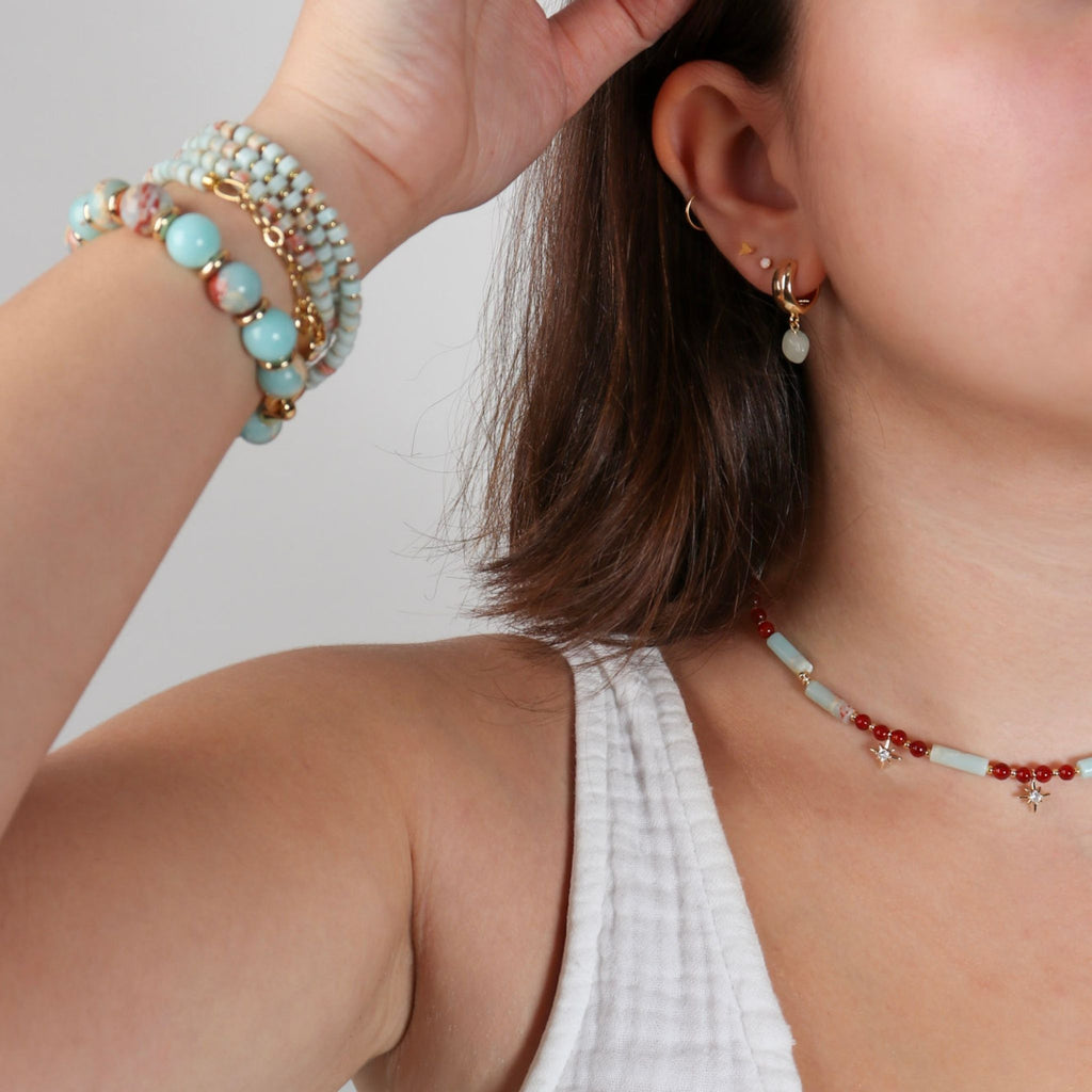 Close-up of a person wearing a beaded bracelet, necklace, and earrings on a neutral background