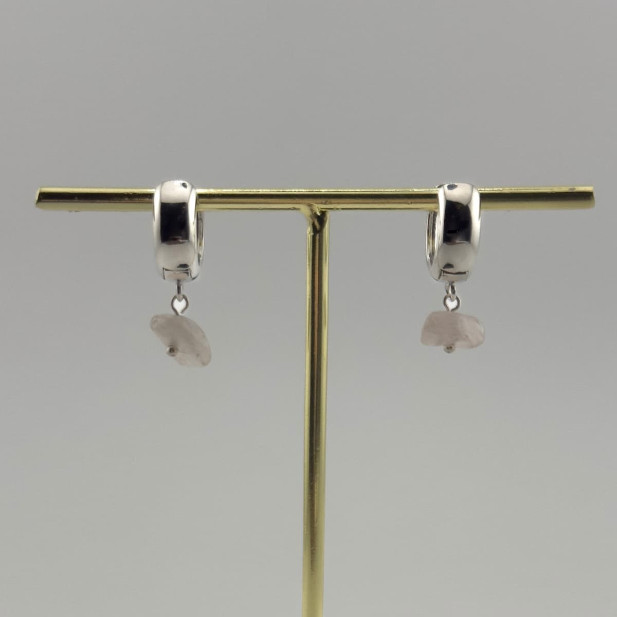 Silver hoop earrings with dangling stones on a gold earring stand against a gray background