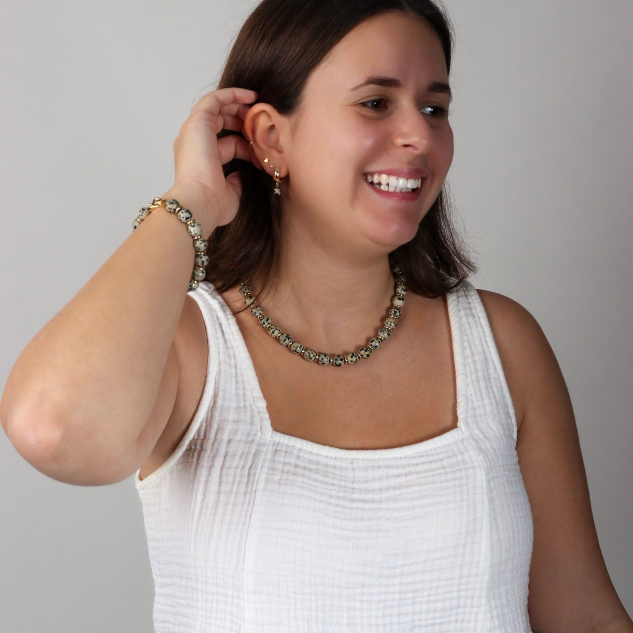 Woman wearing a white sleeveless top and jewelry, smiling against a plain background