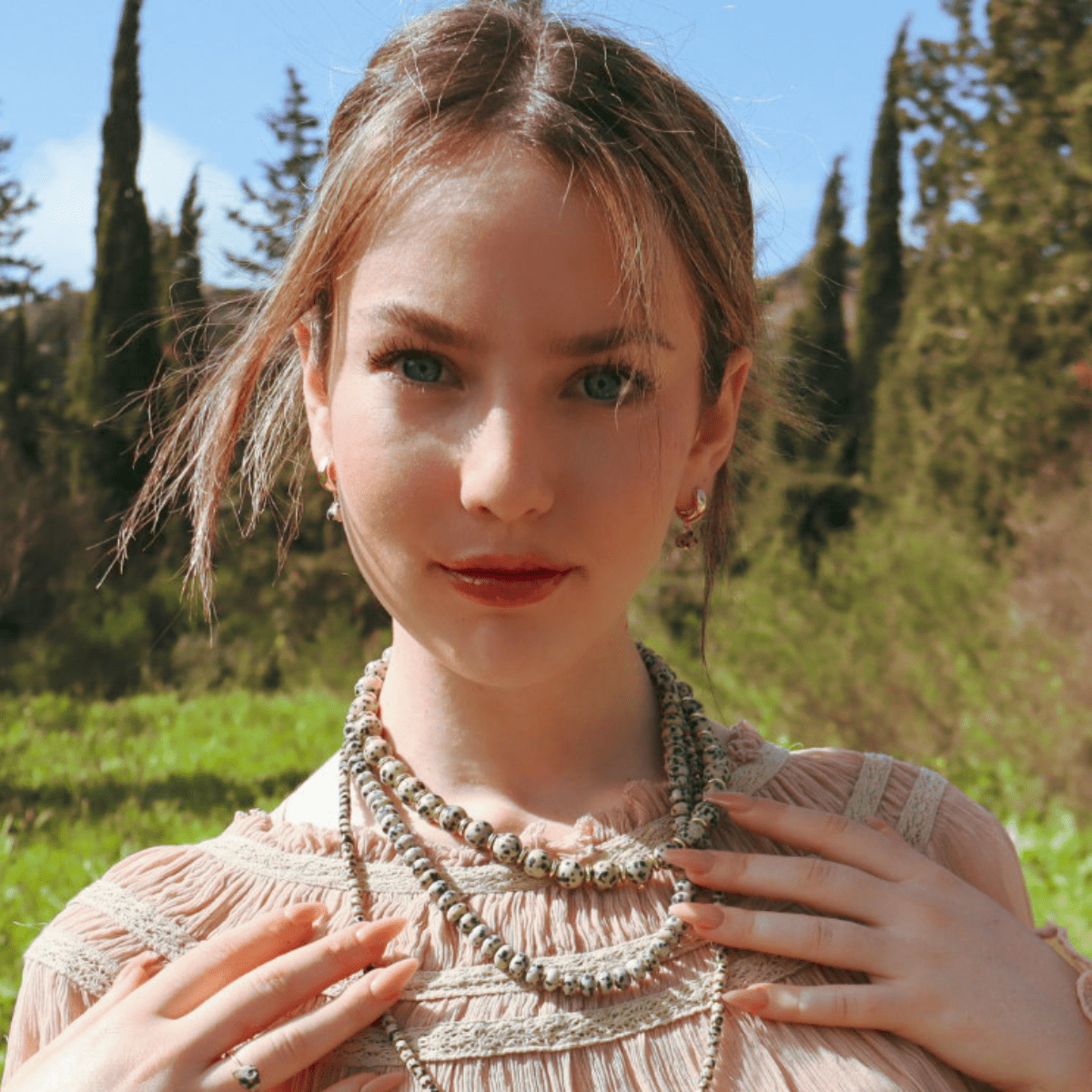 Woman wearing a necklace outdoors with greenery in the background