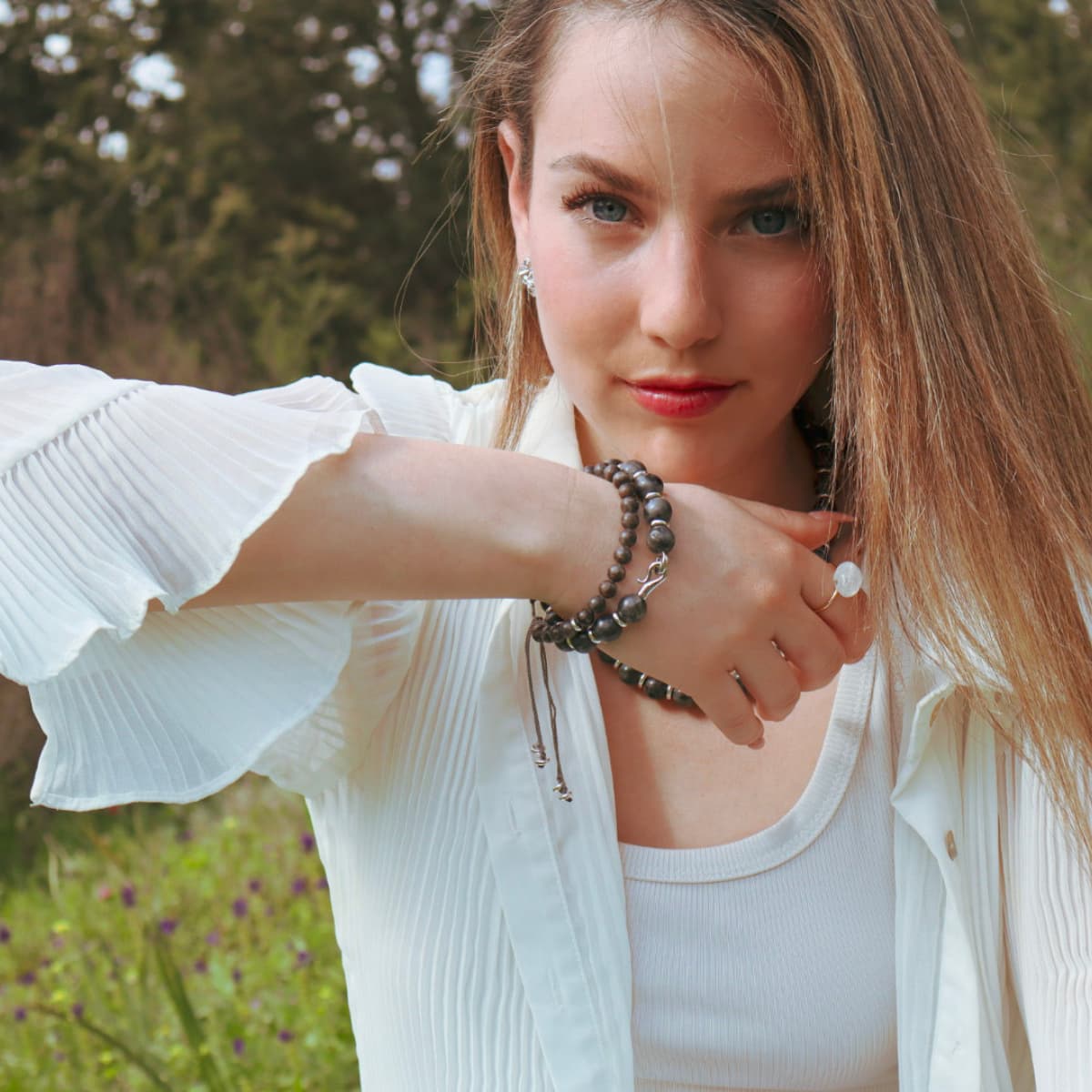 Woman wearing a white cardigan and bracelets outdoors with a blurred natural background