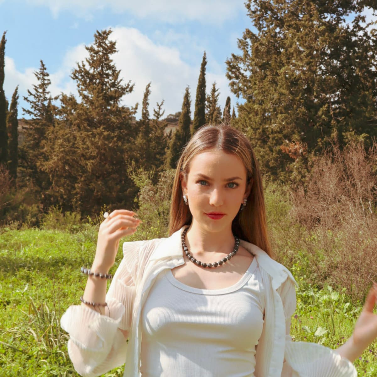 Woman in a white outfit sitting in a grassy field with trees in the background