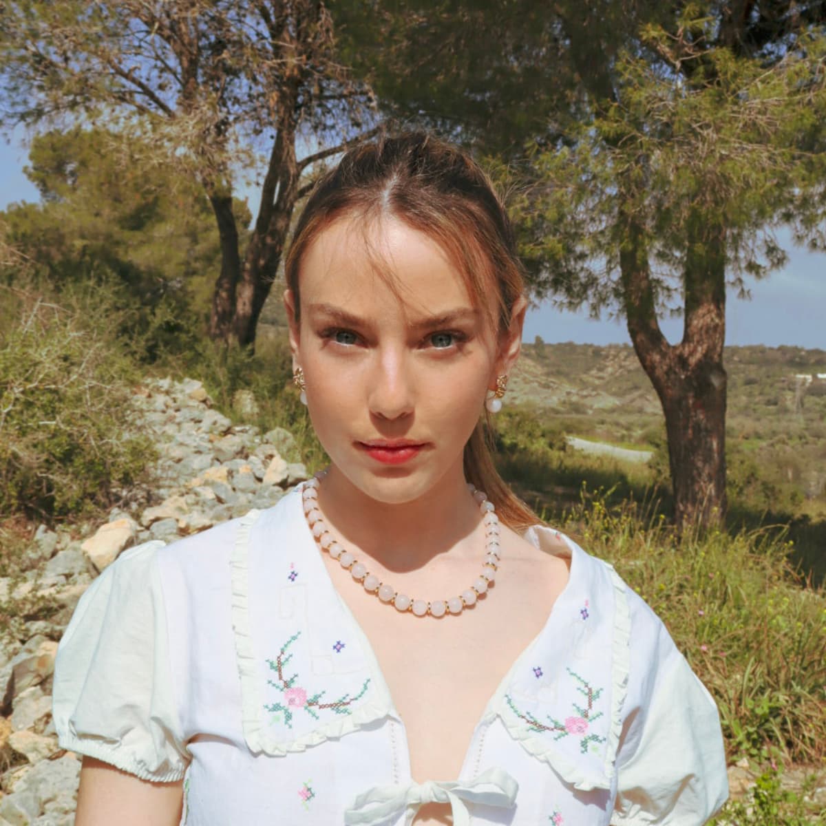 Woman wearing a white embroidered dress with a pearl necklace in a natural setting