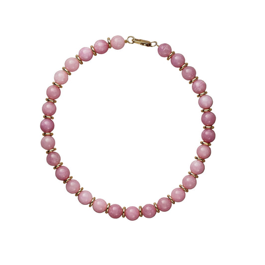 Pink beaded bracelet with gold accents on a beige background