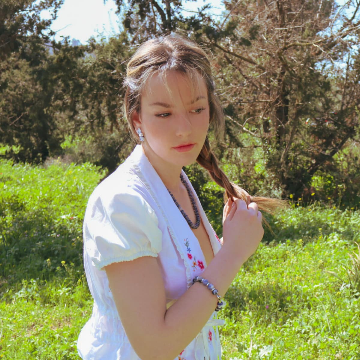 Woman in a white dress standing in a grassy field with trees in the background