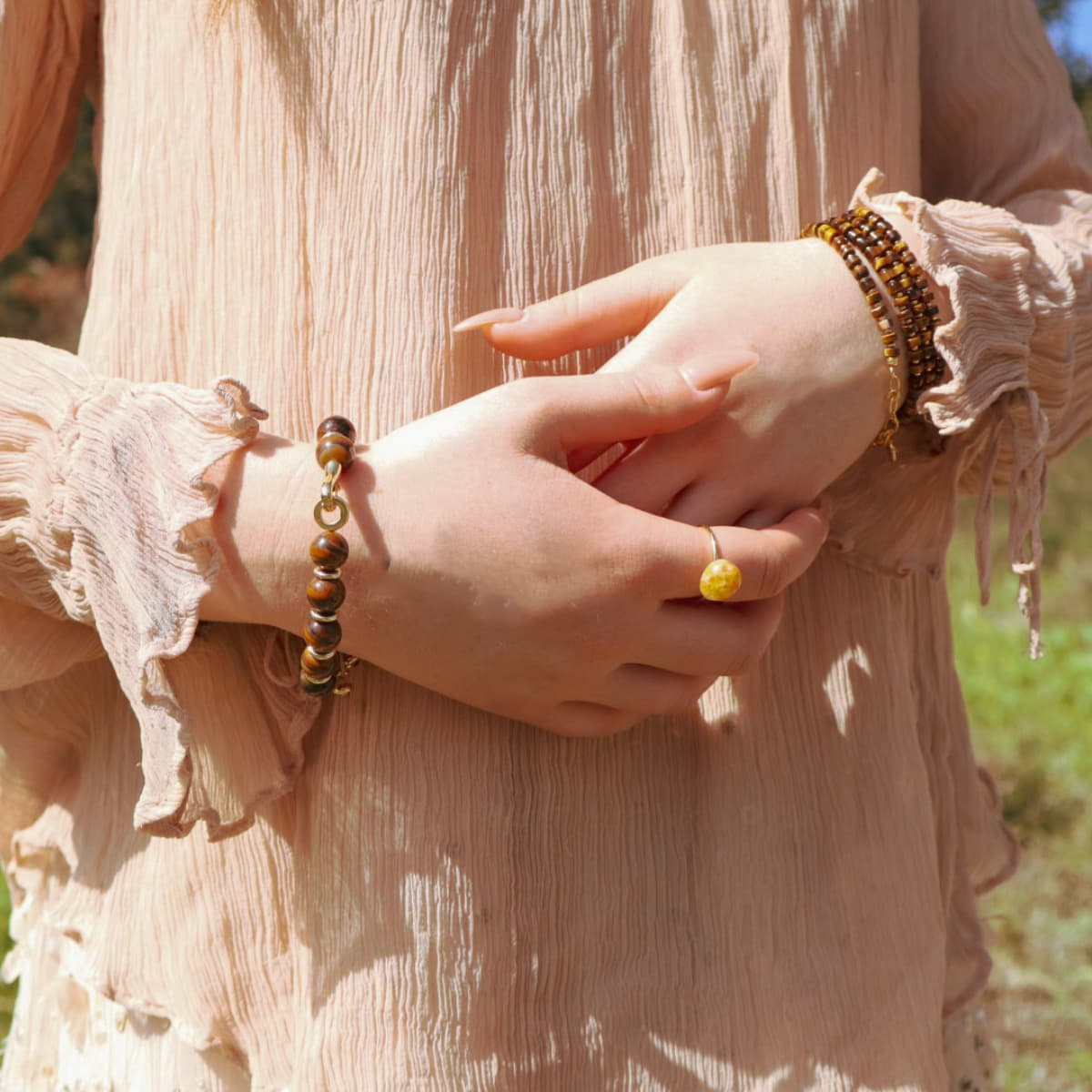 Close-up of hands wearing bracelets and a ring, with a blurred natural background