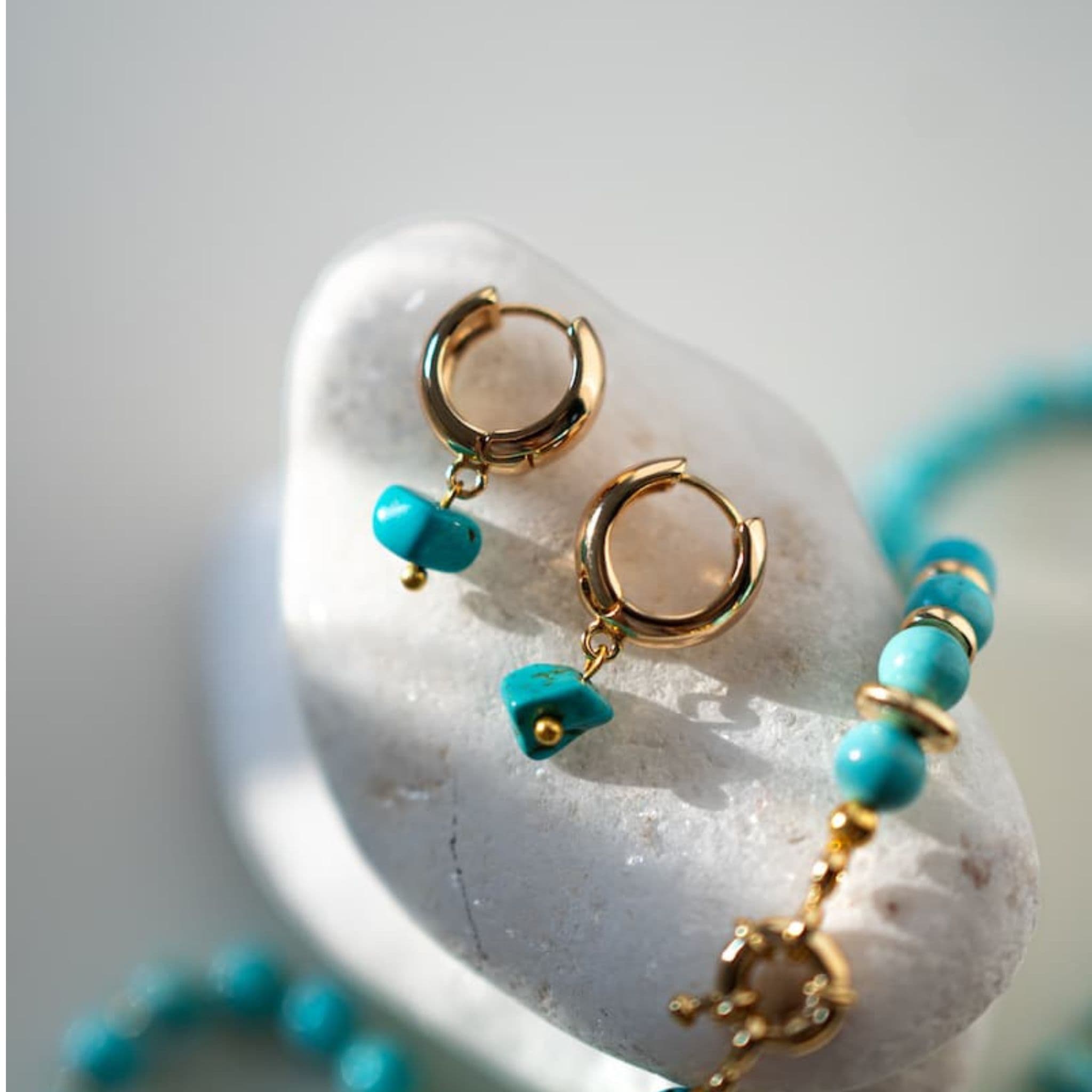 Gold hoop earrings with turquoise beads on a white stone