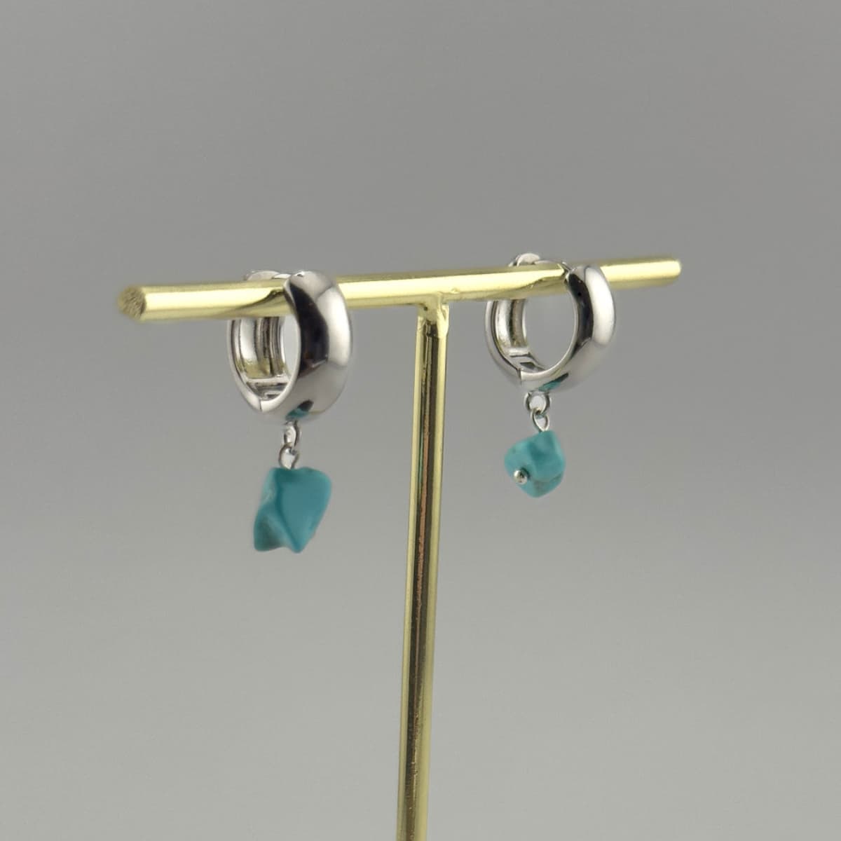 Silver earrings with turquoise stones on a gold stand against a gray background