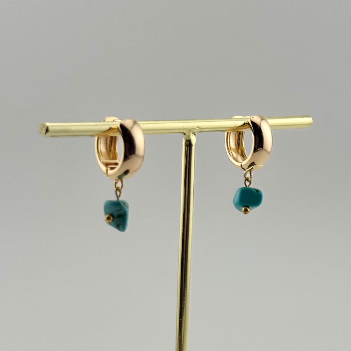 Gold hoop earrings with turquoise stones on a gray background
