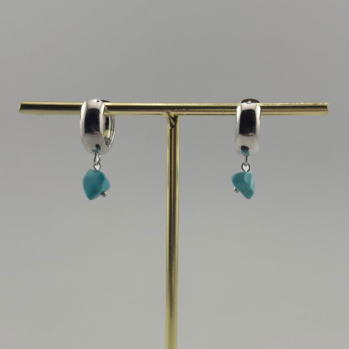 Pair of earrings with turquoise stones on a gold stand against a gray background