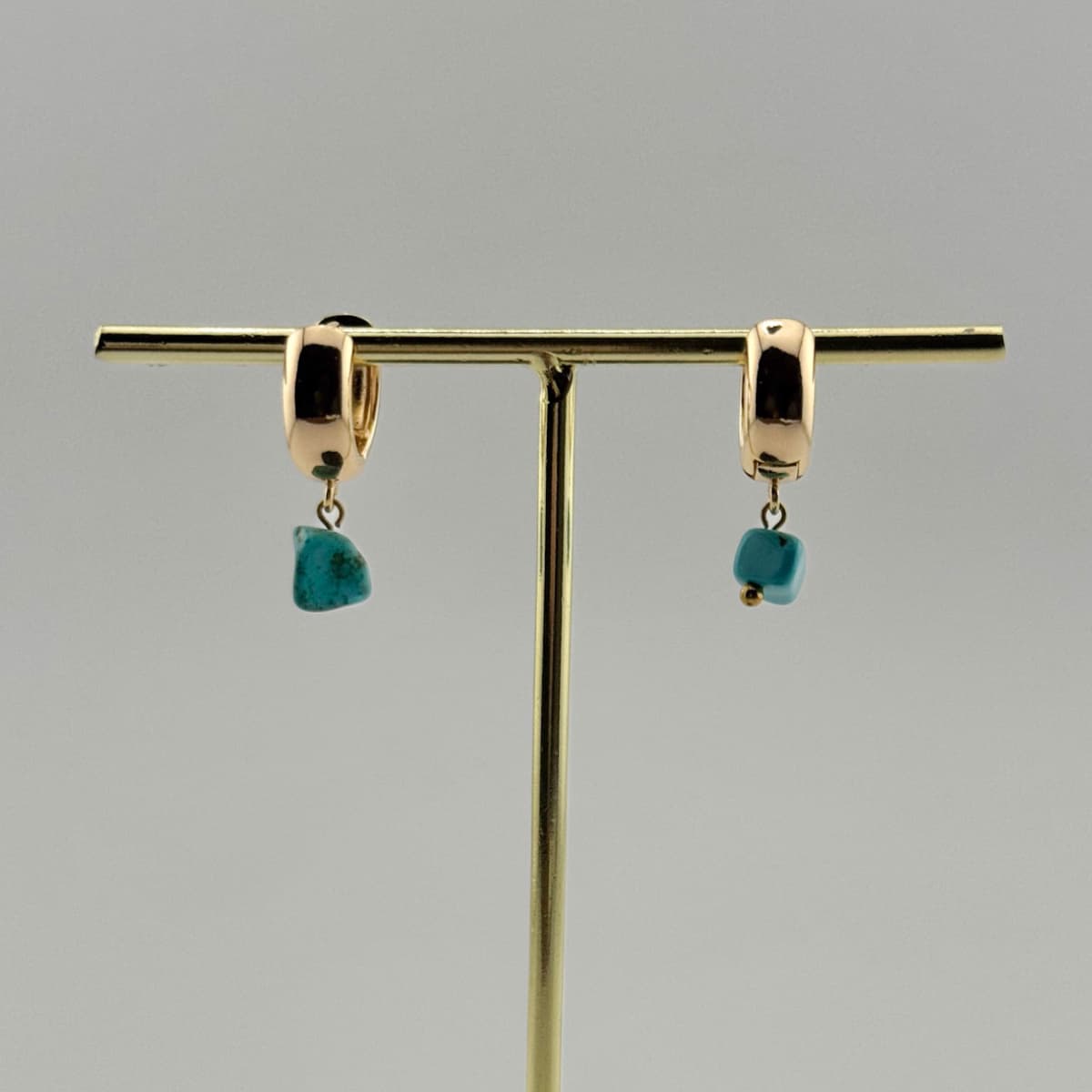 Gold hoop earrings with turquoise stones on a gold stand against a gray background