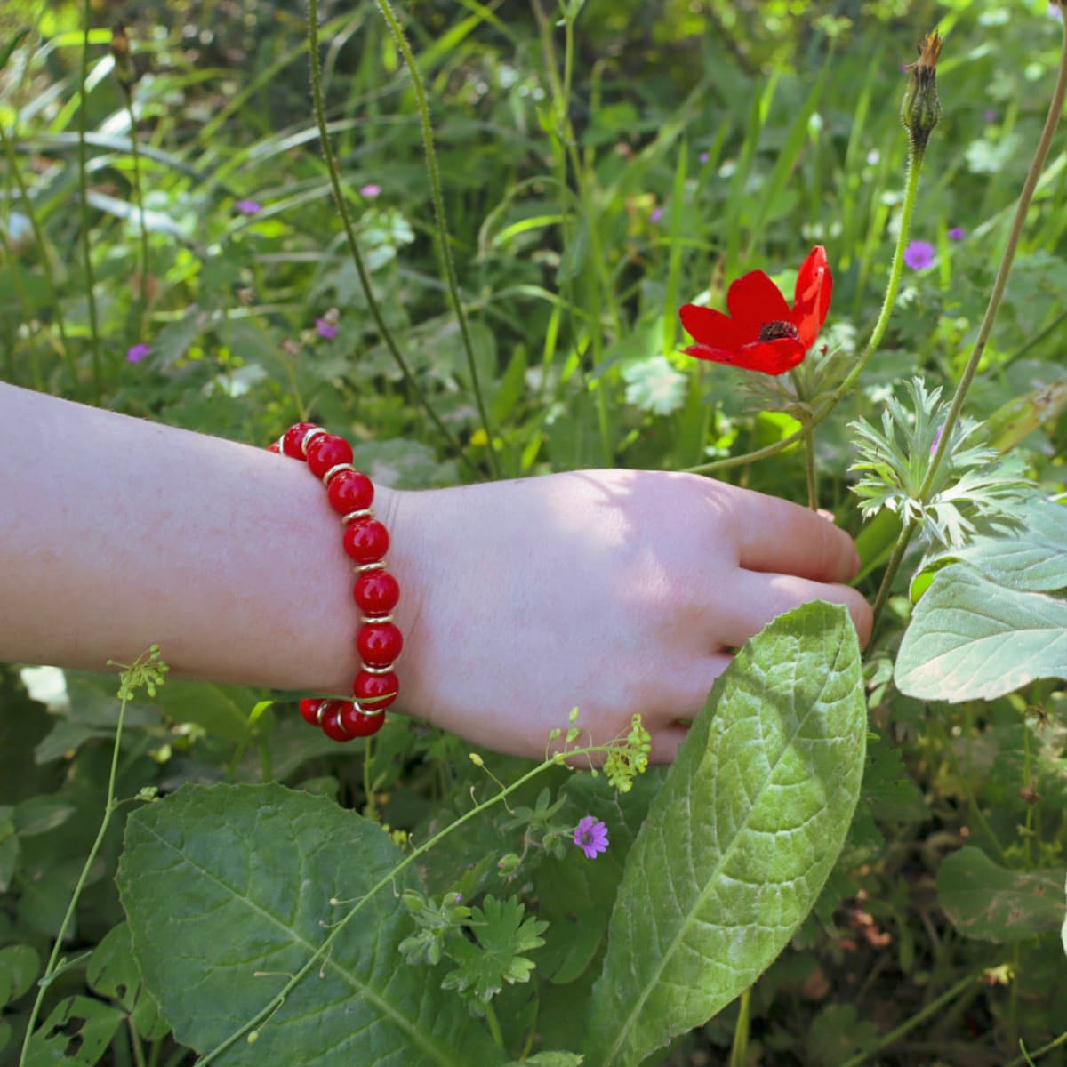 Hand wearing a red beaded bracelet with a red flower in a natural setting