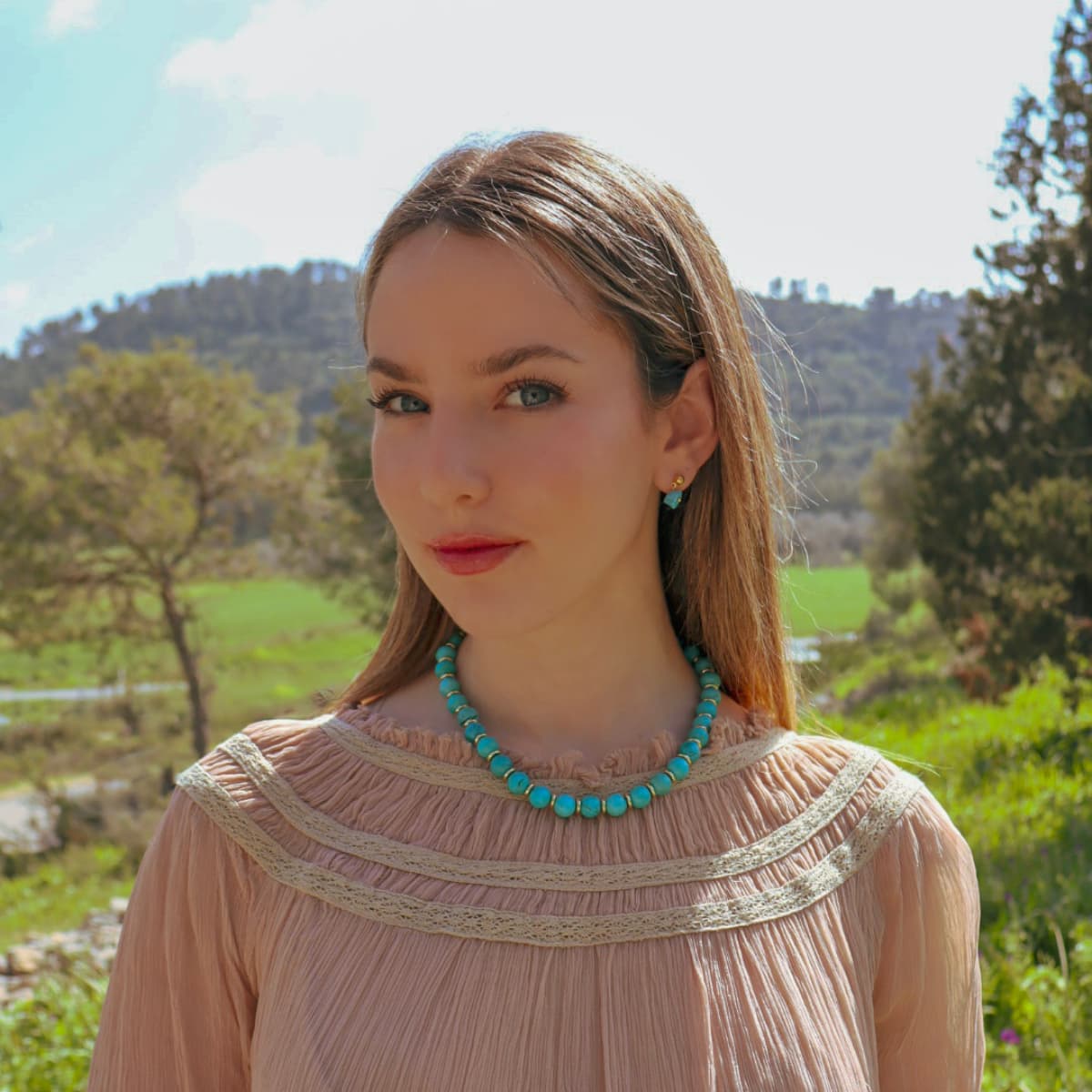 Woman wearing a pink blouse and turquoise necklace with a scenic background